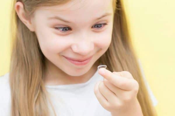 Menina loira, criança com uns 10 anos, olhando uma lente de contato em seu dedo indicador. 