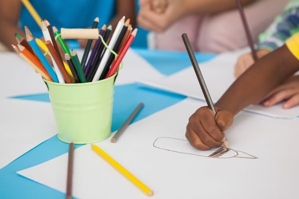 Criança fazendo atividades de pintura frente a um pote cheio de lápis de cores.