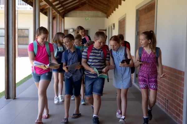 Adolescentes caminham pelos corredores da escola enquanto conversam sobre suas atividades escolares.