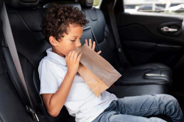 Garotinho negro sentindo-se enjoado após ler um livro enquanto o veículo estava em movimento. Ele segura um saco de papel próximo à boca.