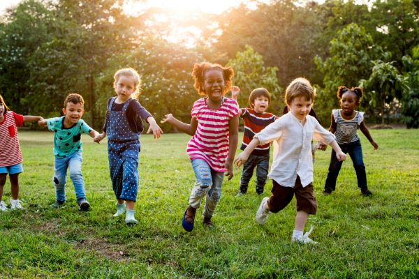 Crianças de diversas etnias brincando ao ar livre em horário apropriado durante o verão.