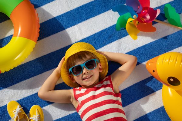 Menino aproveitando o verão devidamente protegido do sol por meio do uso de chapéu e óculos solares.