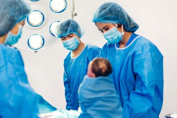 Equipe médica segura bebê recém-nascido, logo após o parto, para encaminhá-lo aos exames de rotina.