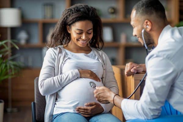 Mulher negra, grávida, realiza o exame pré-natal no consultório do obstetra.
