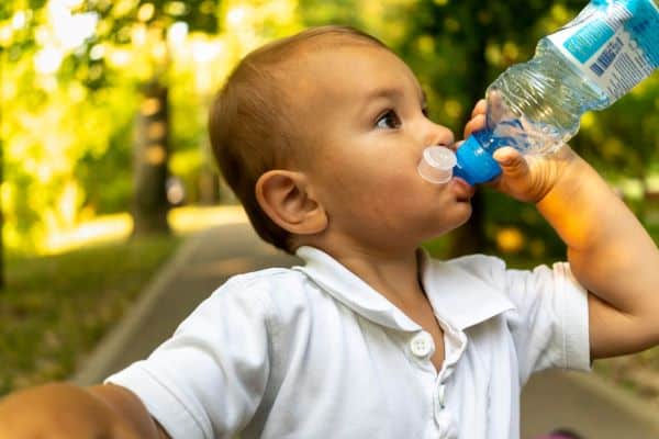 Garotinho de uns 2 anos bebe água no parque e uma garrafa de plástico. A hidratação faz parte de uma alimentação equilibrada.
