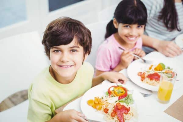 Um menino e uma menina sorriem enquanto se alimentam de forma saudável no refeitório da escola.