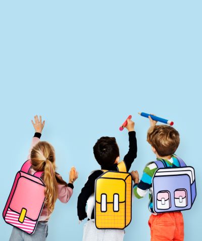 Três crianças em idade escolar, dois meninos e uma menina, desenham com canetões uma parede azul. em suas costas estão desenhos de mochilas, uma alusão à volta às aulas.