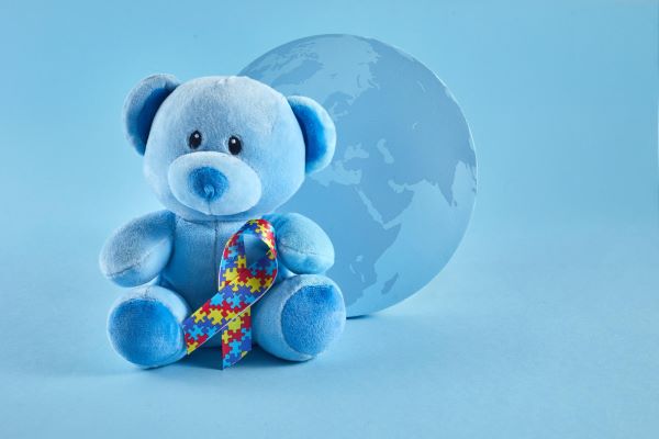 Conceito de conscientização mundial sobre o autismo com um ursinho de pelúcia segurando uma fita representativa da luta autista (quebra-cabeça colorido).