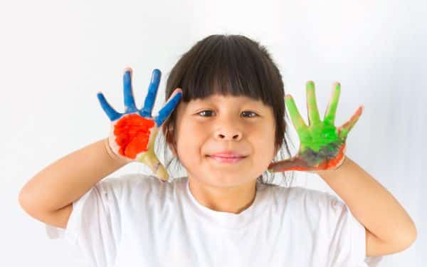 Retrato de menina que apresenta os olhos levemente estrábicos, uma das características do autismo, e as mãos pintadas com as cores representativas da luta autista.