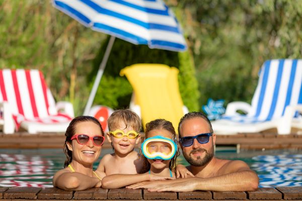 Família feliz se divertindo nas férias de verão na beira da piscina. Os pais protegem-se dos raios uv com óculos de sol, os filhos (menininho e garota) usam óculos de natação.