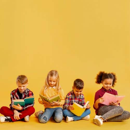 Crianças de diferentes etnias, sentadas no chão frente a um fundo amarelo, leem livros infantis. São 2 meninas e 2 meninos.