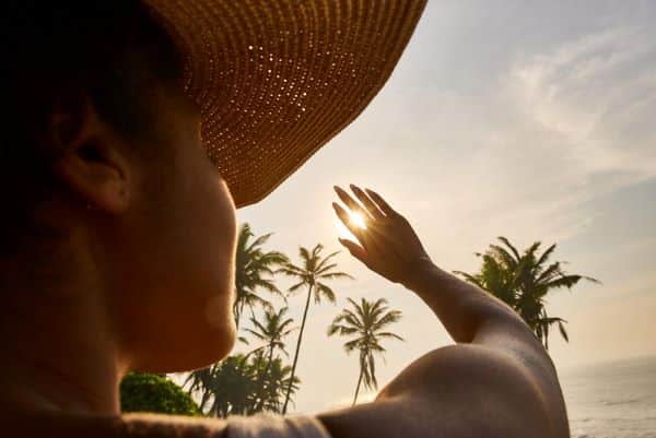 Silhueta de uma mulher, que usa chapéu , esticando a mão e cobrindo o sol para proteger os olhos.