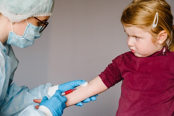 Menina pequena olhando para técnica de enfermagem enquanto faz exame de sangue.