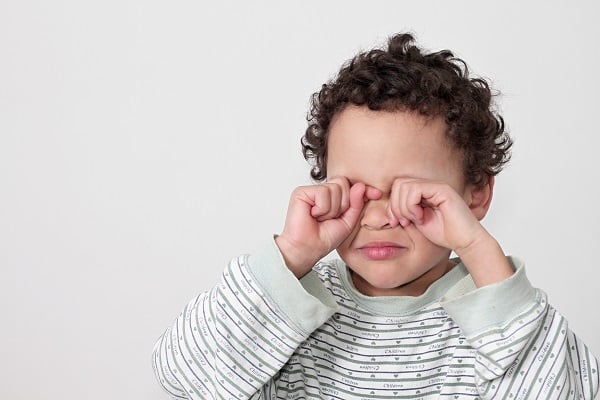 Garotinho de cabelos escuros cacheados, coça os olhos com as duas mãos. Coceira ocular intensa é um dos sintomas das conjuntivites alérgicas.