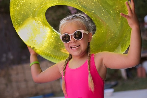 Menina sorridente, usando óculos de sol, maiô rosa e segurando uma bóia, sorri divertindo-se na piscina.
Uma das possíveis lesões oculares está relacionada à queimadura da córnea por falta de proteção ocular.