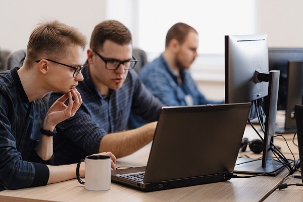 Grupo de jovens programadores que trabalham no escritório frente a duas telas.