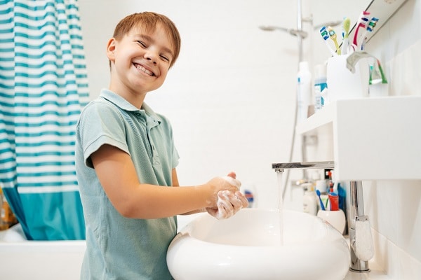 Menino sorridente, pré-escolar , lavando as mãos com sabão debaixo da torneira . A higiene adequada ajuda a manter a saúde ocular infantil.