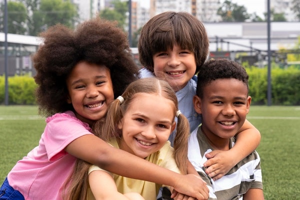 4 crianças sorridente, de diferentes raças, brincam numa praça.