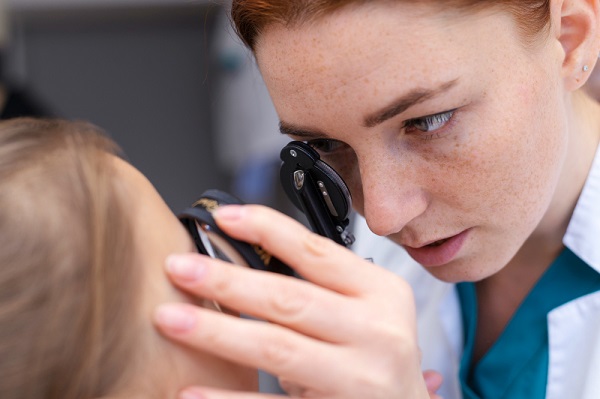 Médica oftalmologista testando a visão do paciente infantil com instrumento oftalmológico.