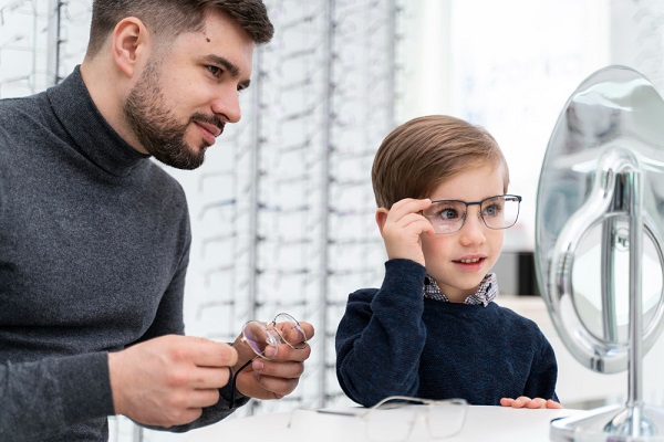 Menino e pai em uma ótica experimentando óculos de grau infantis.