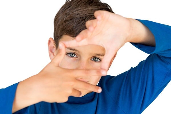 Garoto vestindo camiseta azul enquadra os olhos com ambas as mãos.